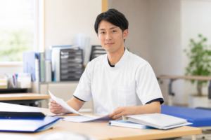 オフィスのデスクで書類を整理しながら、落ち着いた表情で前を向いている医療従事者の姿